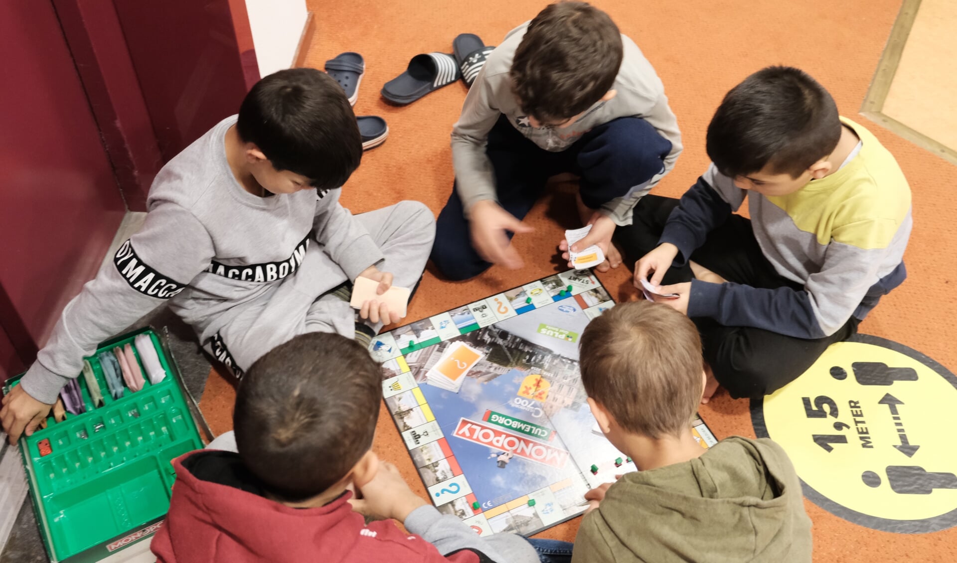 • Op de grond in de hal spelen de kinderen gewoon een Nederlands potje Monopoly.