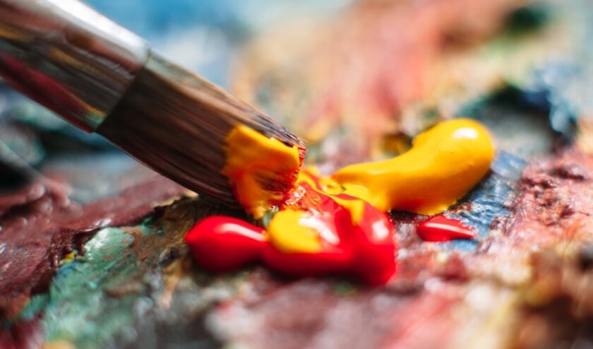 Painter mixes yellow and red oil paint on the palette. Closeup of paint mixing process in art workplace.  