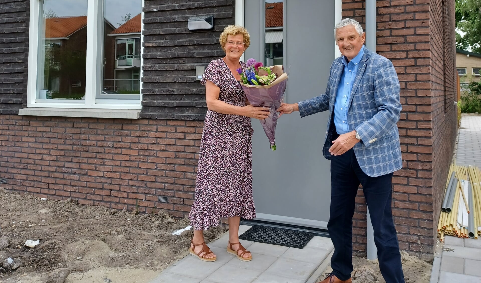 Wethouder Leon de Wit feliciteert mevrouw Visser, één van de nieuwe bewoners, met een bos bloemen.