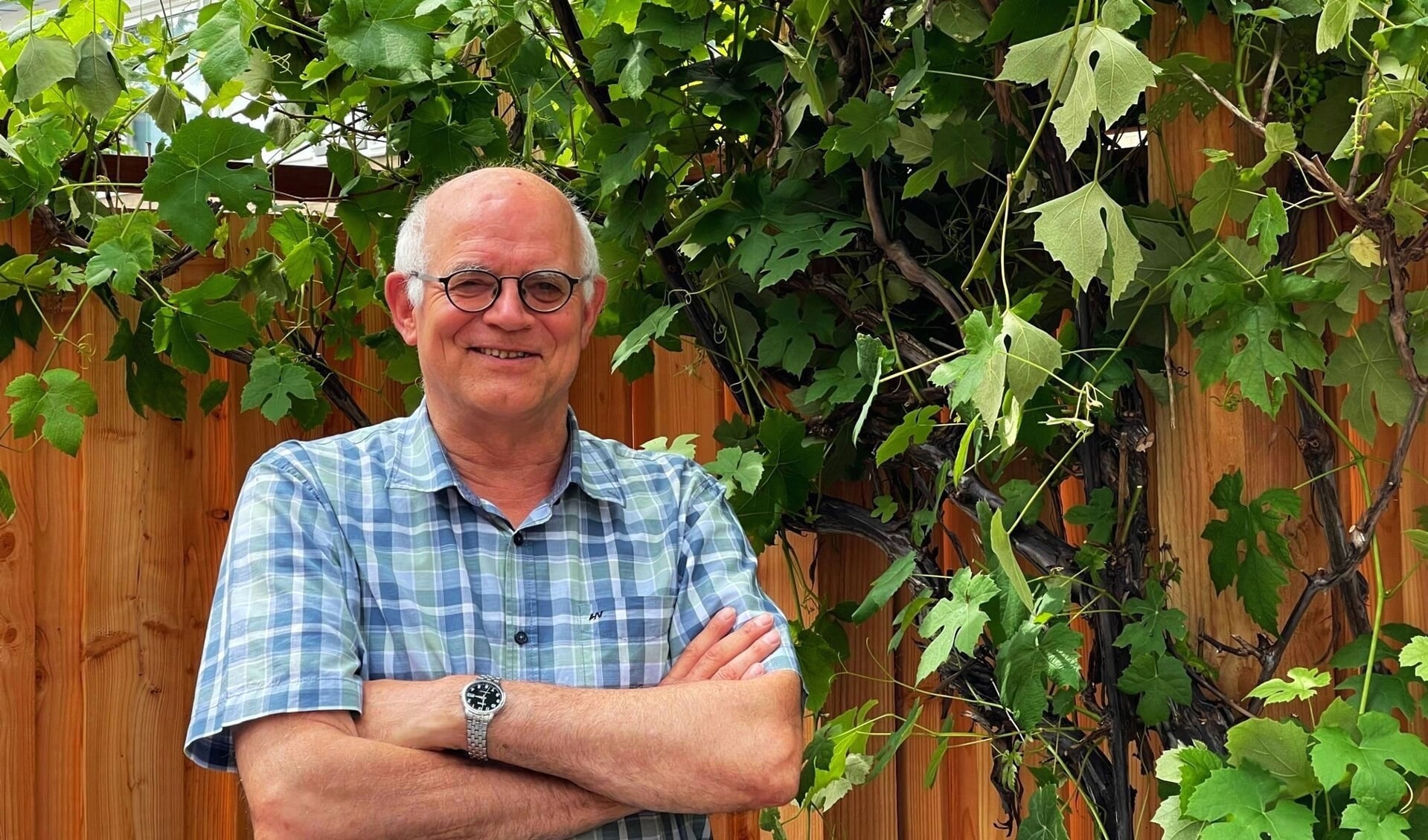 • Emeritus dominee Peter van der Schans, op een geliefd plekje in zijn tuin: onder de bloeiende druivenranken, waar hij en echtgenote Martha vaak te vinden zullen zijn.