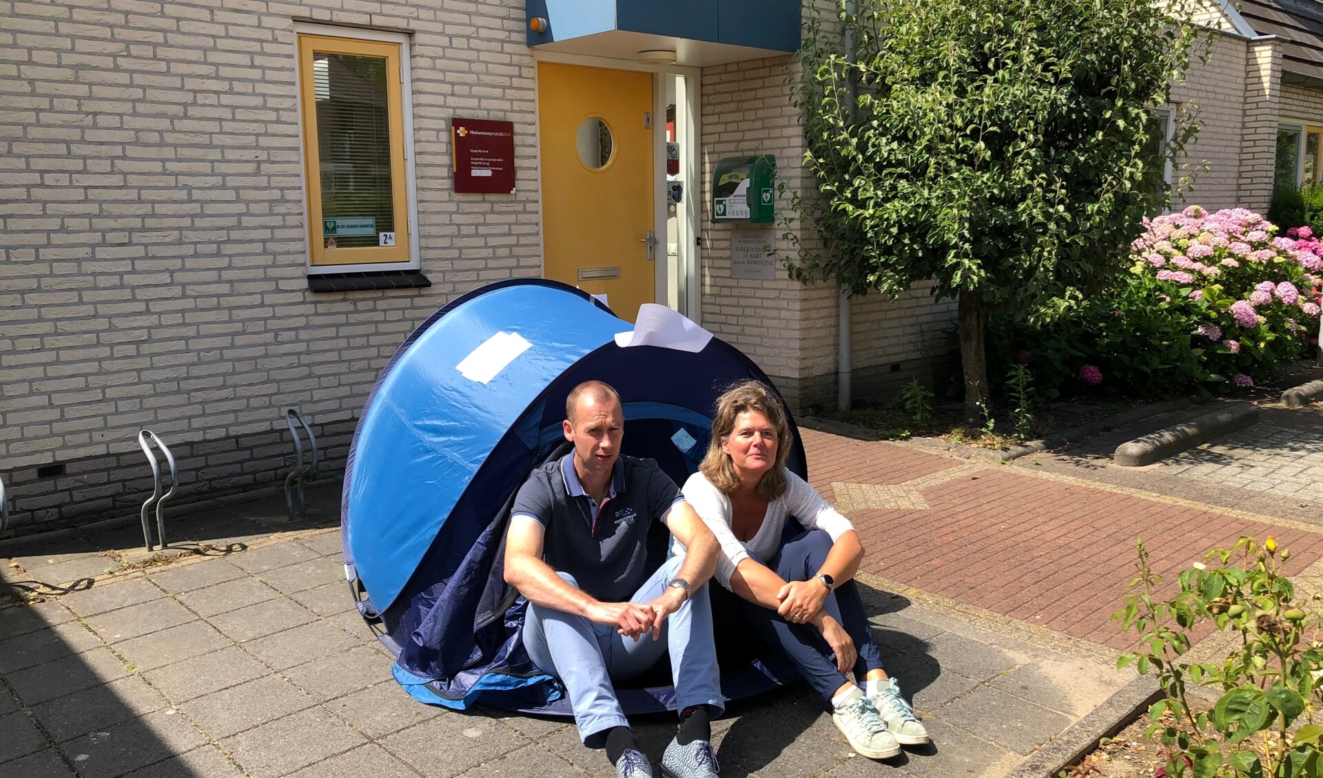 Huisarts Schaafsma en vd Voort vd Kleij van Huisartsenpraktijk Deil voor de tent (als symbool voor hun krappe huisvesting). 