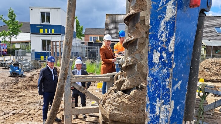 Wethouder Martine de Bas draait de eerste paal de grond in bij de start van de bouw van tien sociale huurwoningen. Wethouder Pieter Neven en Thius-directeur René Wiersema kijken toe.