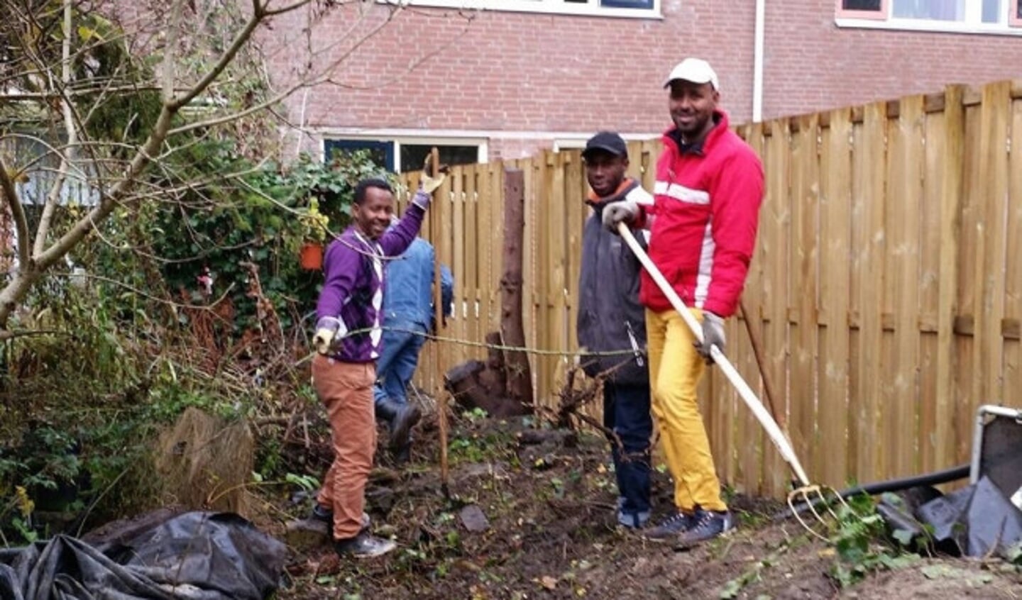  Vier AZC-vrijwilligers aan het werk in een tuin.