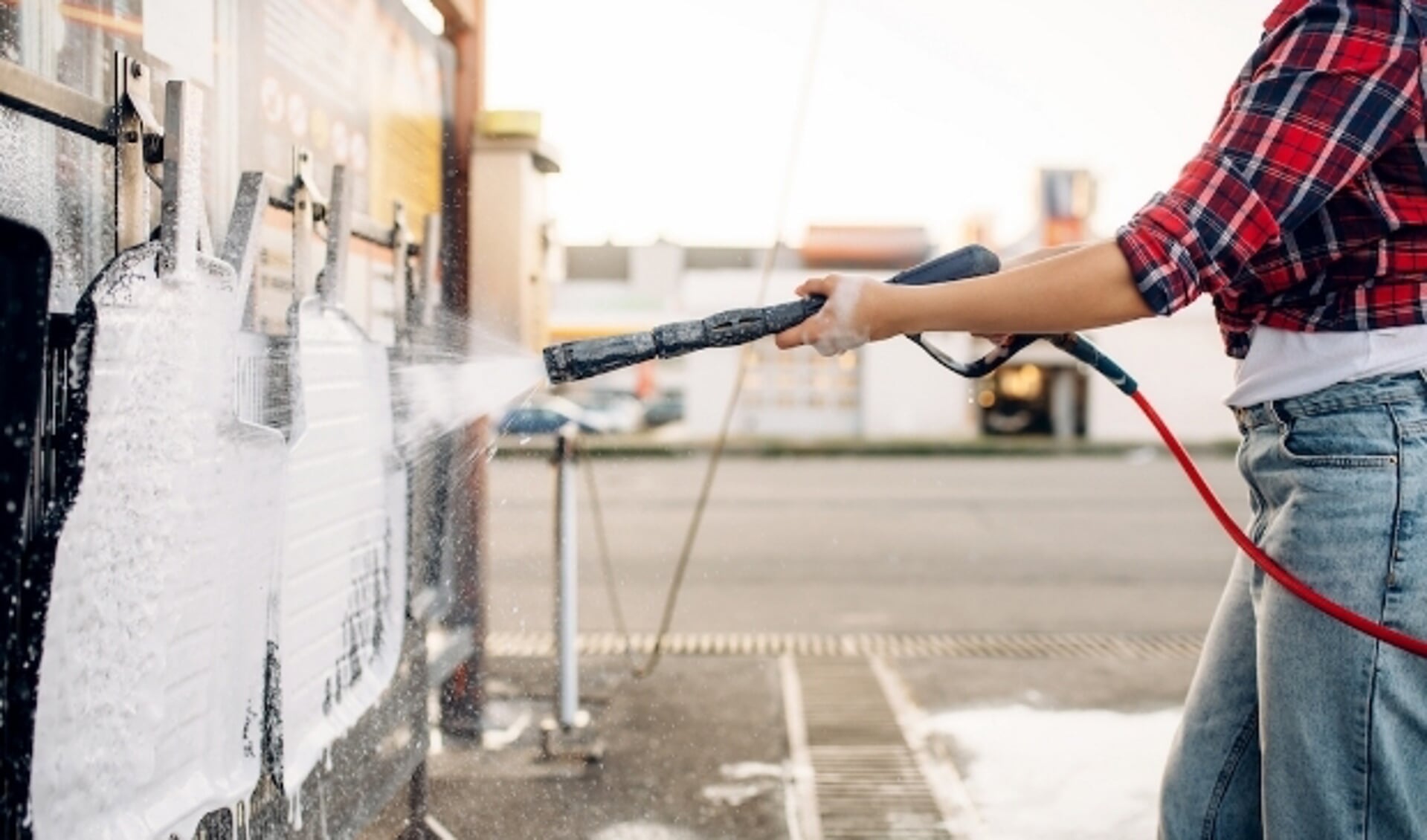 Female person with high pressure water gun in hands cleans car mats, touchless carwash. Young woman on self-service automobile washing. Outdoor vehicle cleaning at summer day