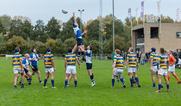 <p>Een line-out: RC Zwolle (blauw-wit) komt net niet hoog genoeg. Op de achtergrond het Zwolse clubhuis.</p>