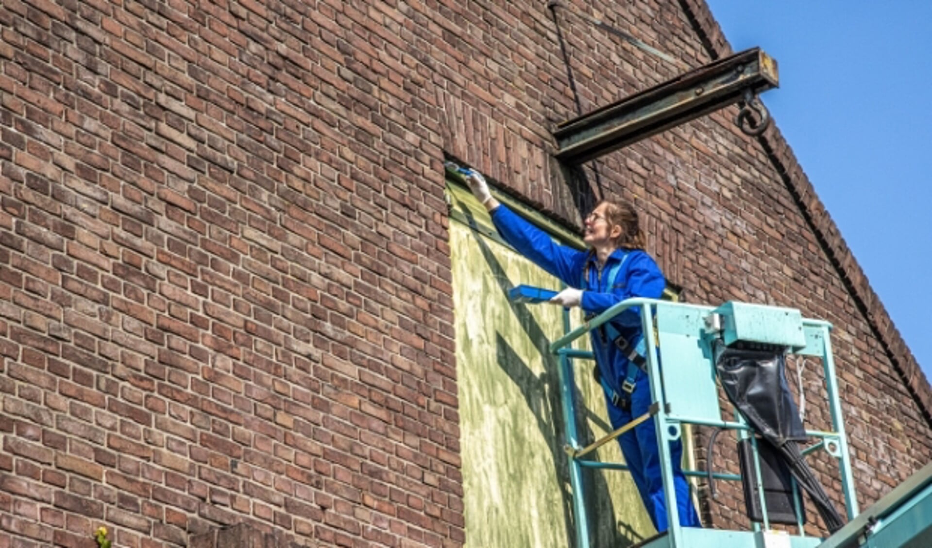 Adrienne Heemstra  op de hoogwerker. De oude veehallen aan de Grote Baan krijgen een verfbeurt.  