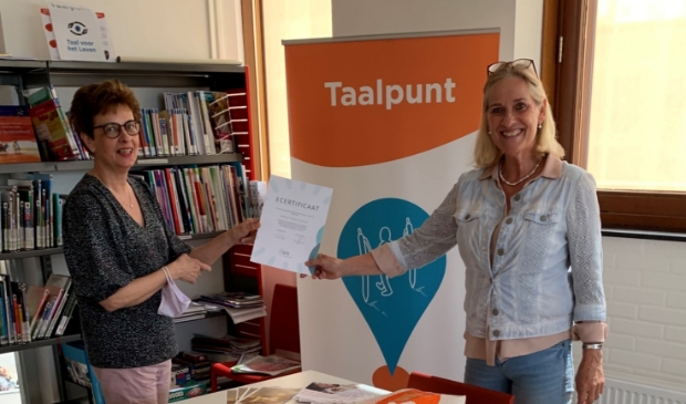 Bibliotheekdirecteur Hetty van de Weg en Taalpuntdocent Barrie Nitrauw tonen trots het behaalde certificaat