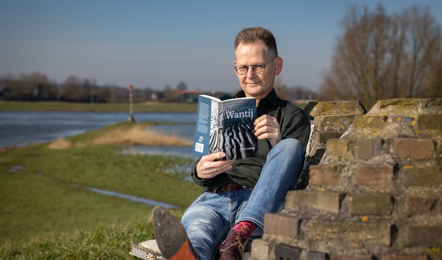 Dick Laning met zijn roman bij de IJssel. Hij maakt daar veel 'gedachtenloopjes' voor zijn schrijfwerk.