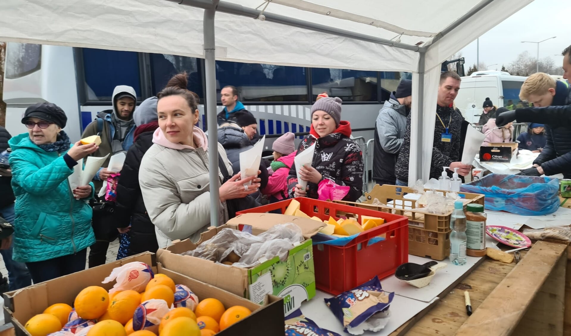 Vluchtelingen staan in de rij voor een zak patat, vlees, kaas en fruit.