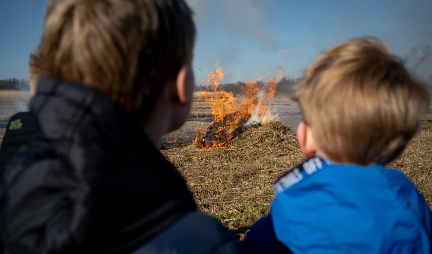 Kinderen kijken naar brandend rietafval. 