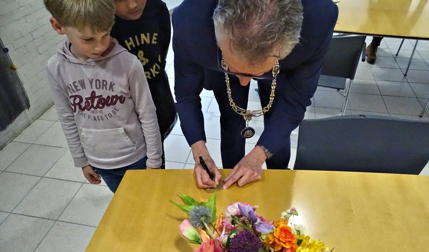 De burgemeester tekent het label; Ties kijkt nauwlettend toe.