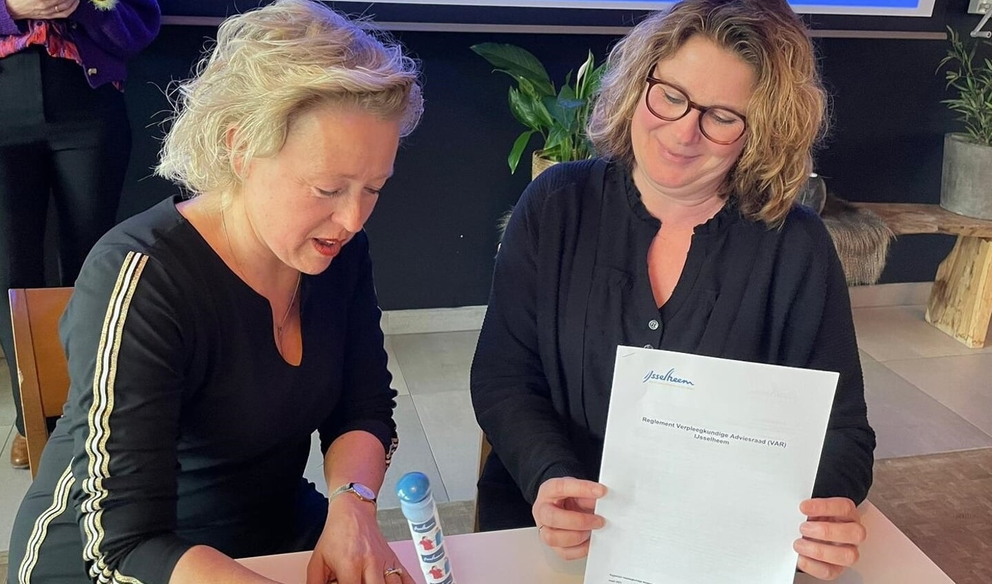Karin Leferink, raad van bestuur IJsselheem (l) en Ivonne Huijsman, voorzitter van de verpleegkundige Adviesraad ondertekenen het formele reglement, waarmee de VAR een feit wordt.