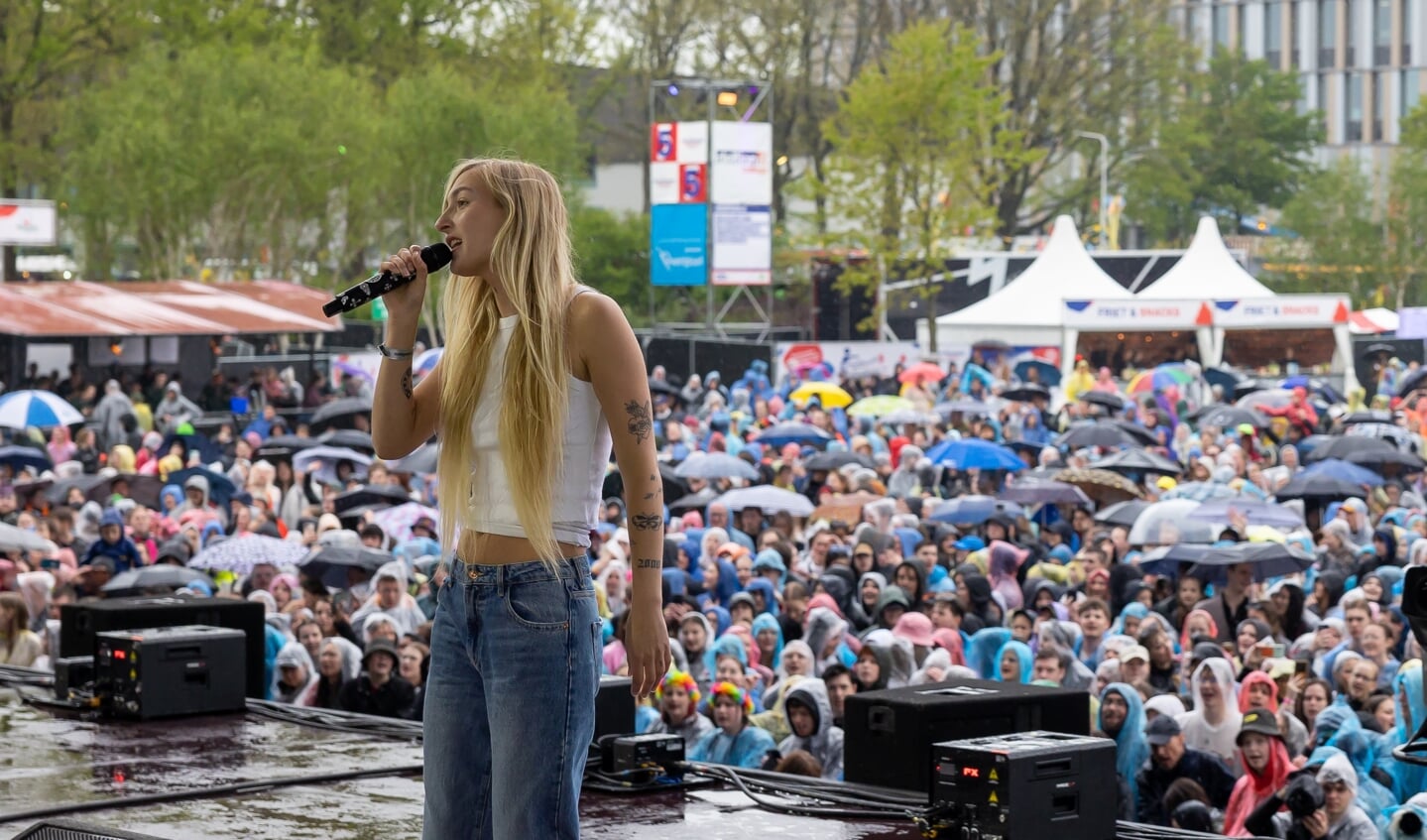 S10 tijdens haar optreden op het Bevrijdingsfestival. In regenkleding en onder paraplu's kijkt het publiek toe. 