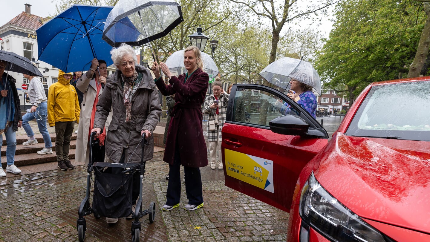 Wethouder Dorrit de Jong probeert de 96-jarige Ger Bos te beschermen tegen de regen. 