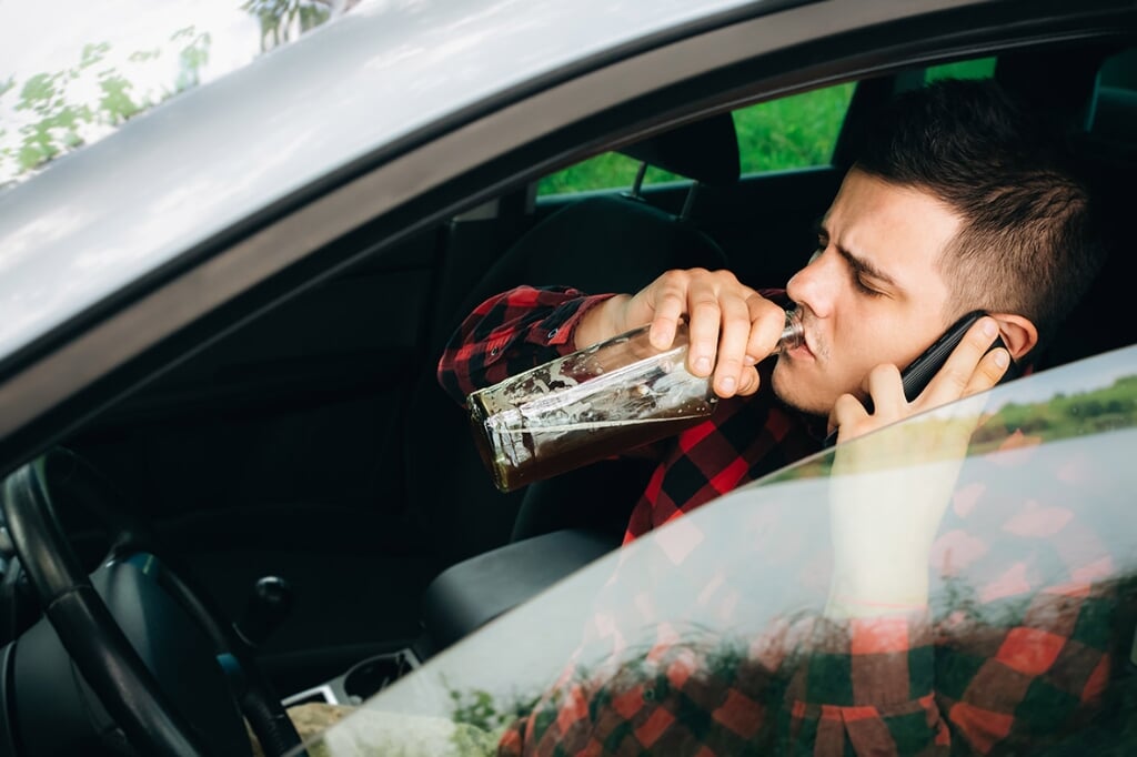 Drunk driver behind the wheel. Man drinking in the car and talking on the phone. Alcohol problem. Dangerous problem. Accident possibility.