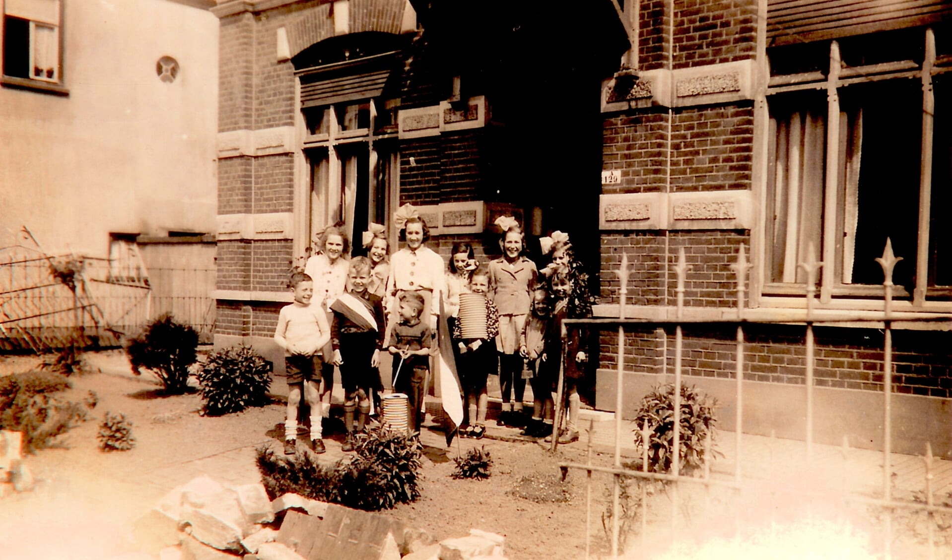 Voor het huis van Cas van Vroonhoven kijken kinderen naar de optocht ter herdenking van de bevrijding in september 1944. Rechts van de deur is het oude adres van vóór 1948 (A129) zichtbaar. (12533)
