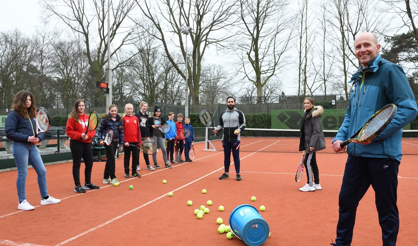 Tennistrainer Koen met op de achtergrond Meike, Ali en de jeugd tijdens de tennisles