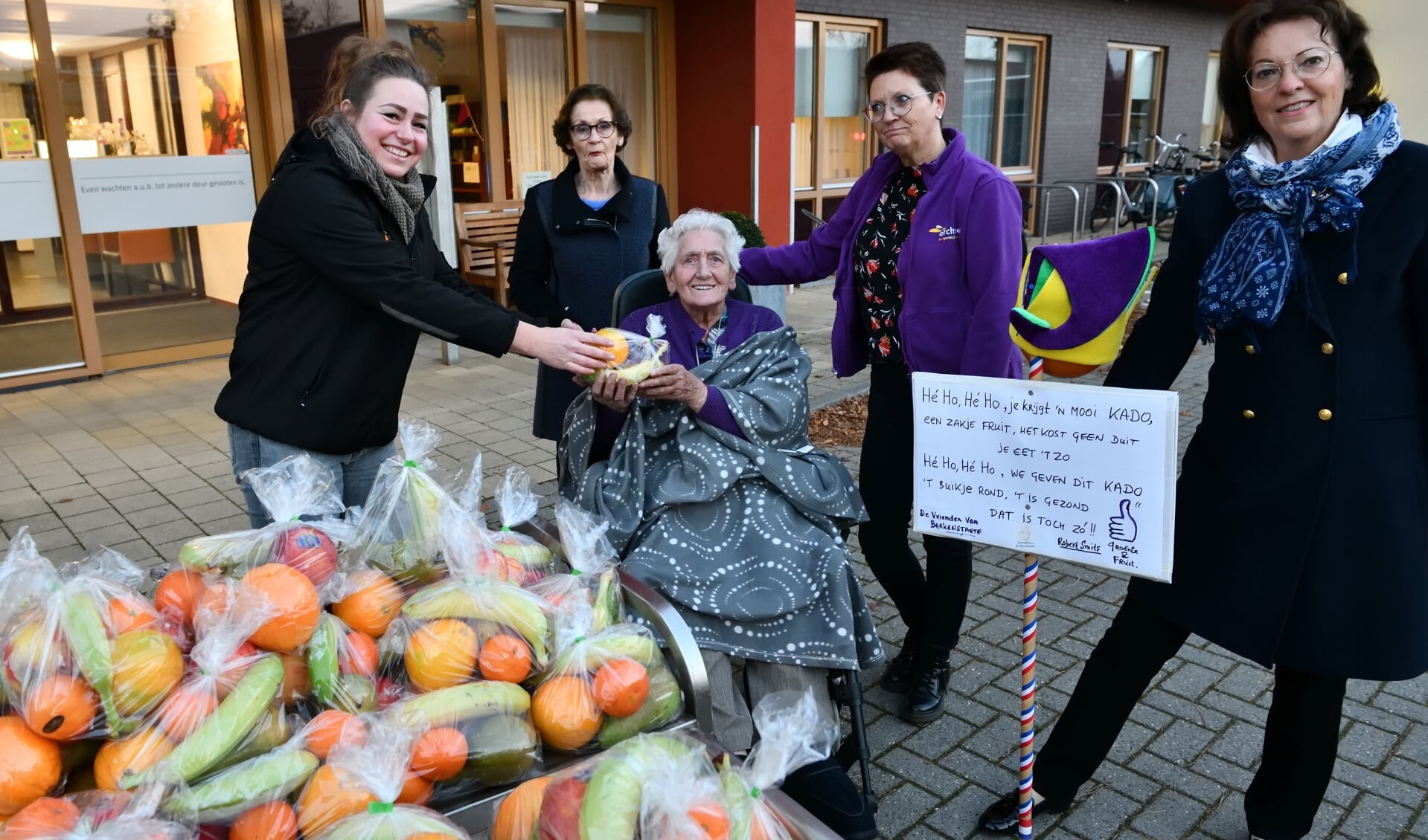 Melanie Schadee overhandigt mevrouw De Haas het fruitzakje in het bijzijn van Elly Speetjes, Hermine Versantvoort en Leny Achten