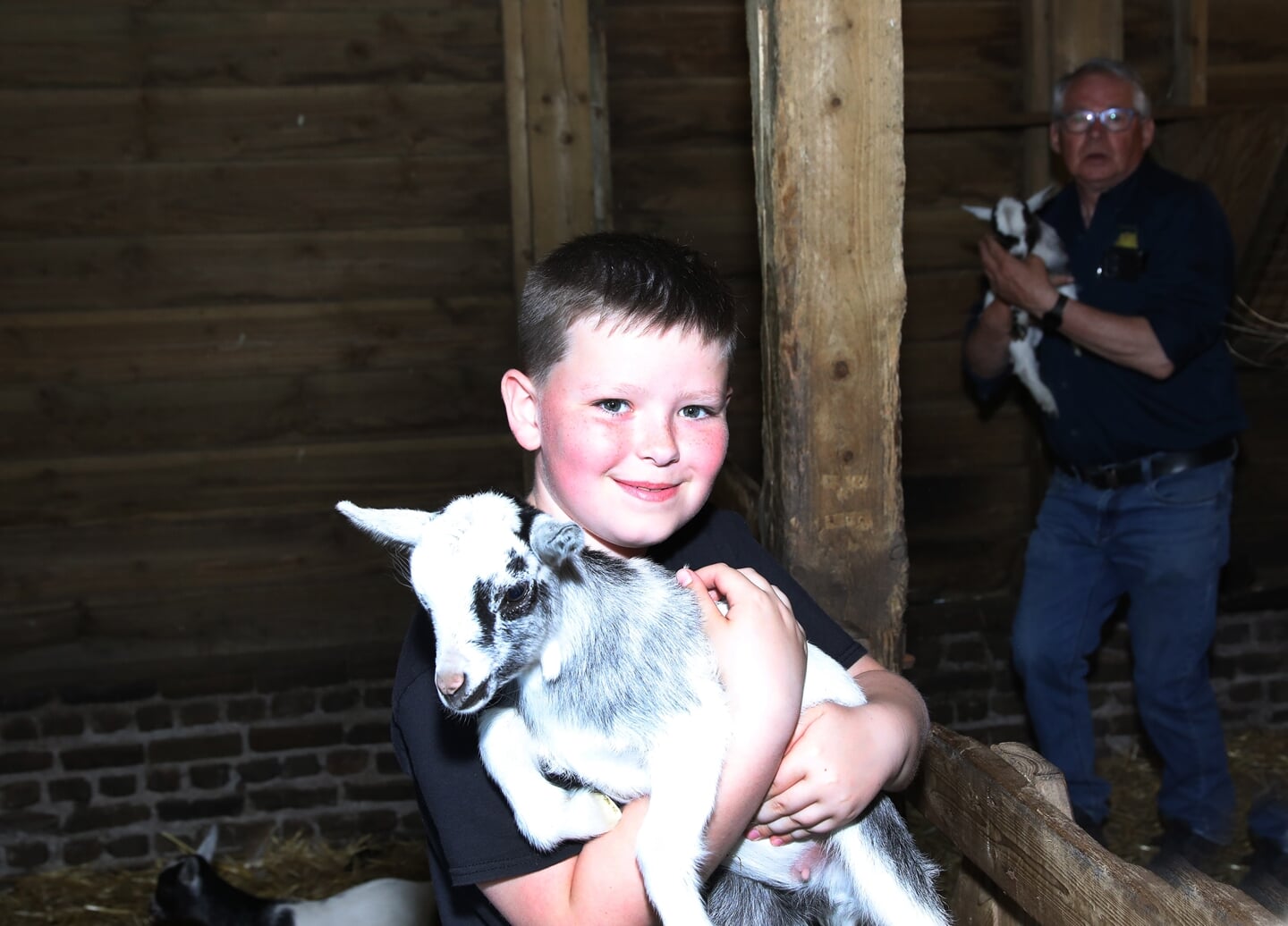 Een van de kinderen houdt een pasgeboren geitje vast, op de achtergrond beheerder Cor Essens