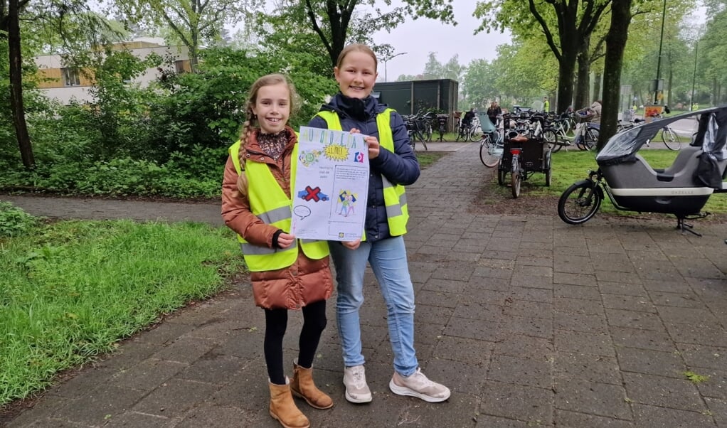 Sophie (links) en Nienke voor hun school De Bloktempel met de poster die ouders vraagt niet met de auto naar school te komen 
