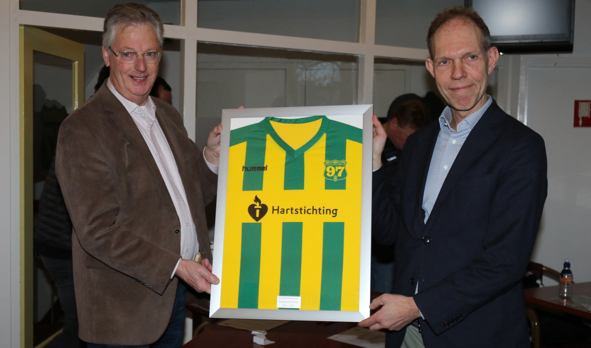 Floris Italianer (r) ontvangt van Ton van Emmerik een ingelijst shirt van de zaterdagselectie met de naam van de Hartstichting. Foto: PR