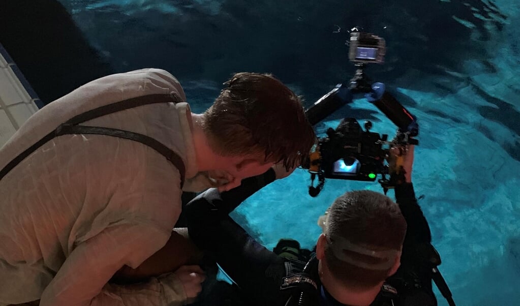 Foto's: acteur Ronald kijkt de beelden terug met de cameraman, opstelling van de set, en regisseur Roobol (met wetsuit) geeft instructies aan assistent Ewoud Abspoel (links) en acteurs Ronald Kanter (wit shirt) en Mike Libanon (rechts).