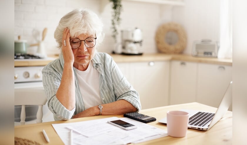 Sad frustrated senior woman pensioner having depressed look, holding hand on her face, calculating family budget, sitting at kitchen counter with laptop, papers, coffee, calculator and cell phone  