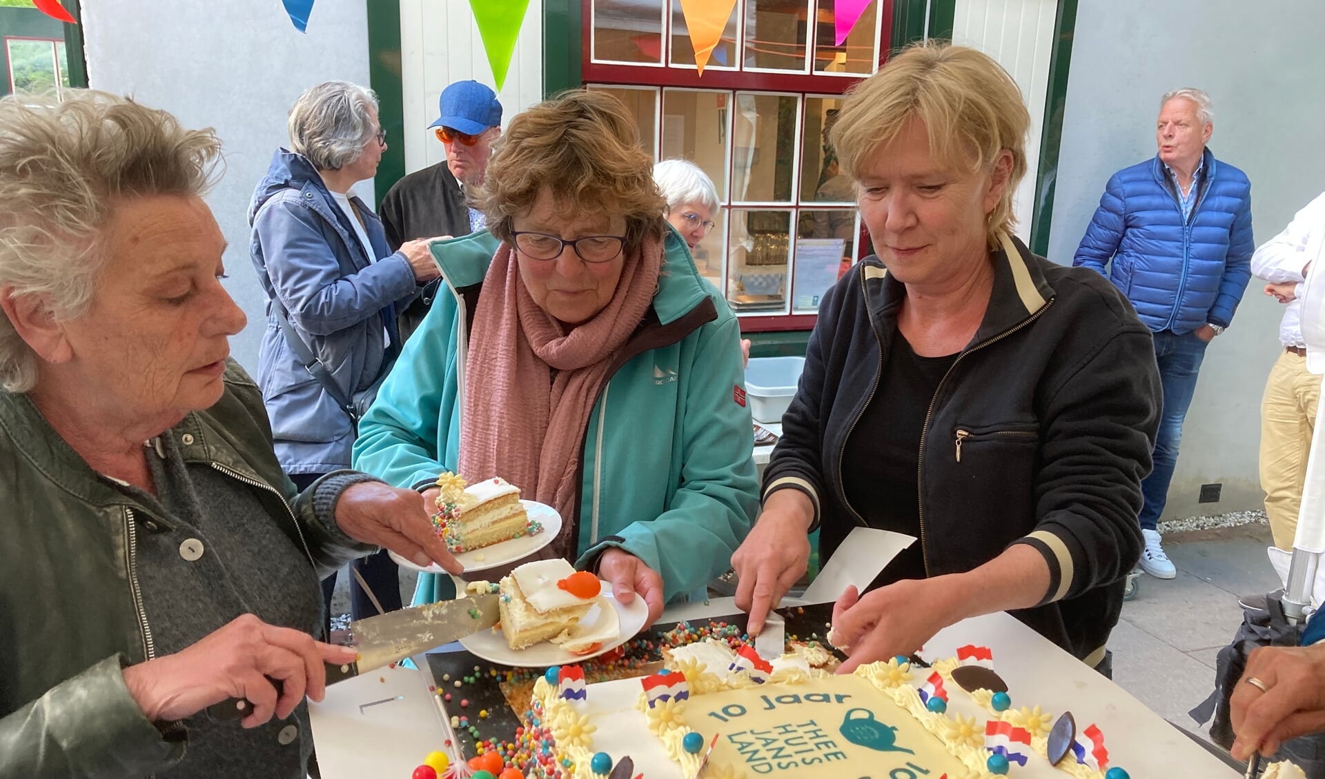 Monique van de meer, Anneke Verhoog en Tanja Kraaijeveld snijden de taart aan die bakker Verhoog bakte voor de vrijwilligers en leerlingen van het Theehuis. 