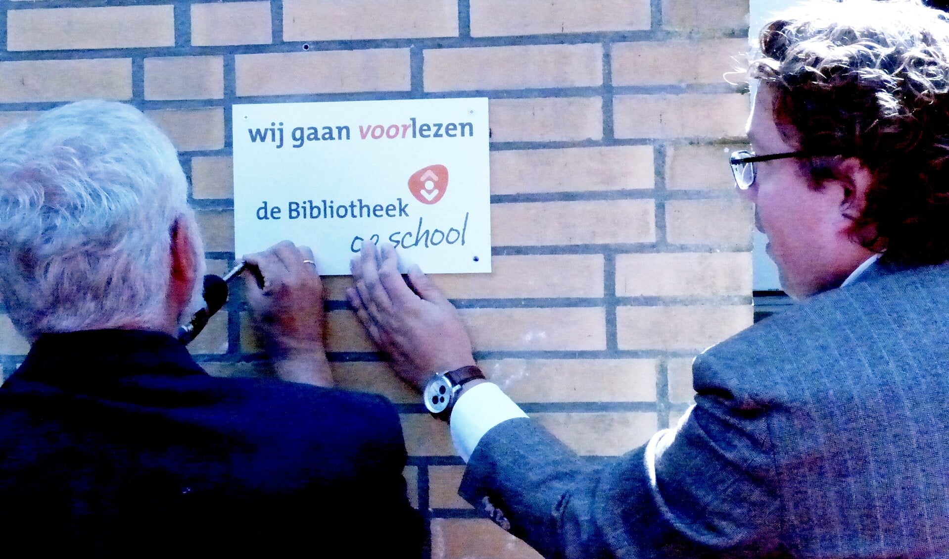 Harm Smit, directeur Bibliotheek aan de Vliet, en Kees Jan Visser, directeur Maerten v.d. Veldeschool bevestigen samen symbolisch het muurplaatje van de bibliotheek op de school.