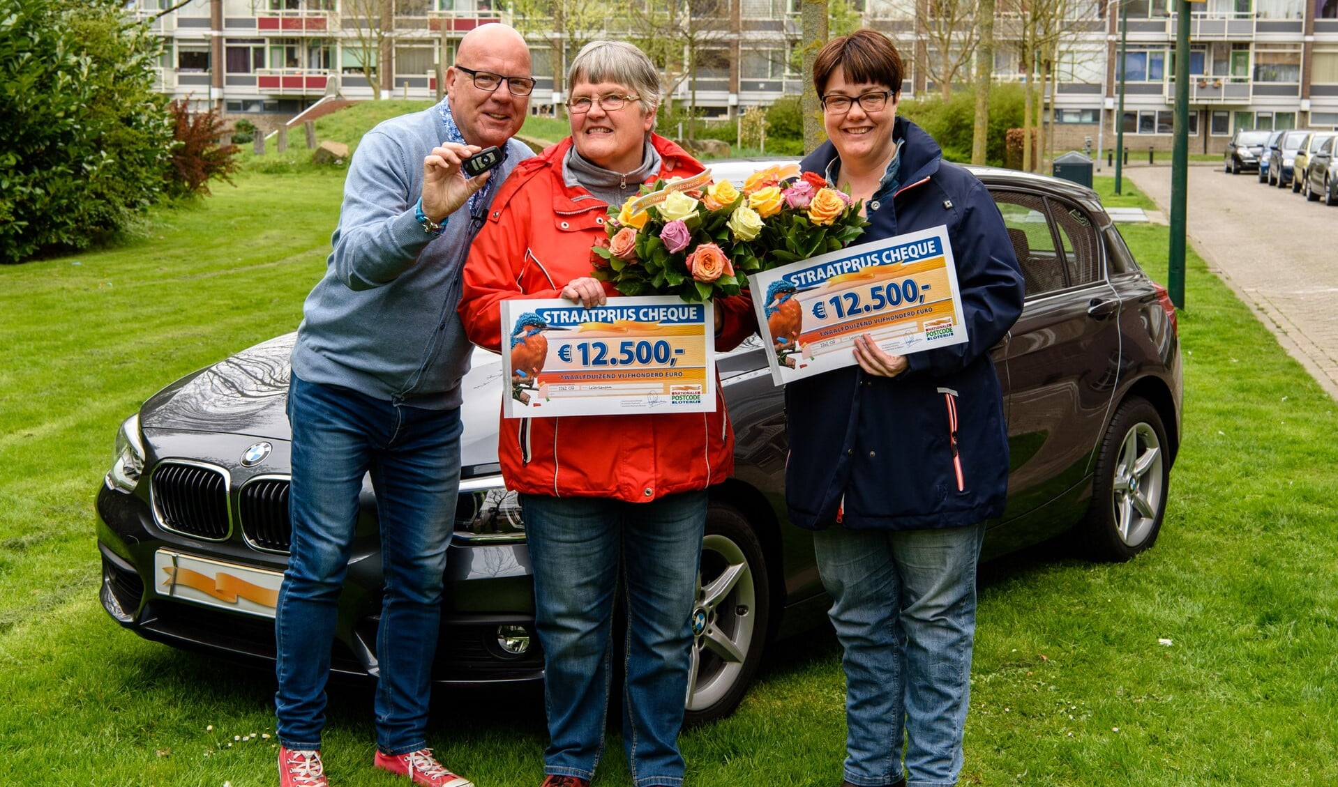 Elly uit Leidschendam wordt, in aanwezigheid van haar dochter Judith, verrast door Postcode Loterij-ambassadeur Gaston Starreveld met de PostcodeStraatprijs-cheque en een BMW (foto: Roy Beusker Fotografie).