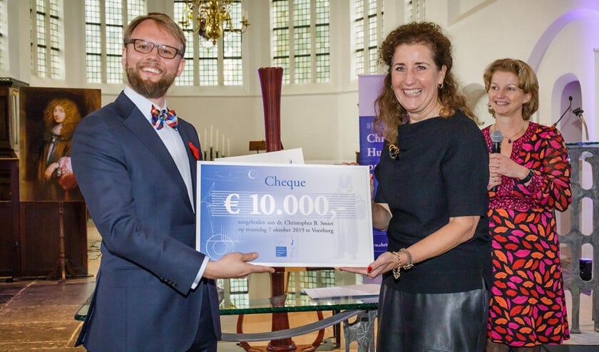 Fotobijschrift: Chris Smiet ontvangt de cheque behorend bij de Christiaan Huygens wetenschapsprijs 2019 uit handen van minister Ingrid van Engelshoven van OCW. Rechts de voorzitter van de Stichting Christiaan Huygensprijs, Marjan van Loon.