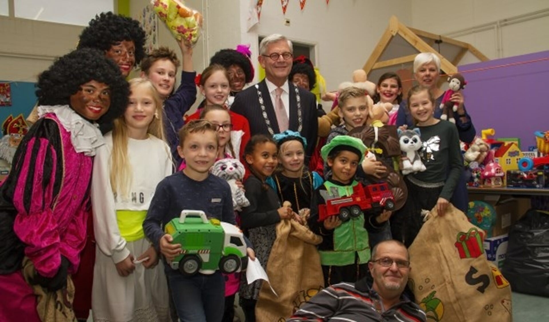 burgemeester met kinderen floriant, juf Hanneke Hoogeveen en liggend Ronald Offers van speelgoedbank IKROS.