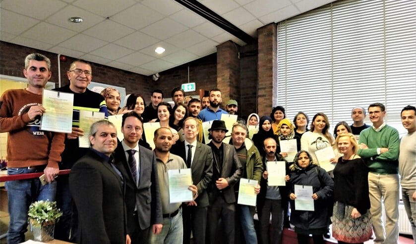 De vluchtelingen tonen, samen met ‘hun’ wethouder, met trots hun participatieverklaring. Daarbij mag de foto natuurlijk niet ontbreken.