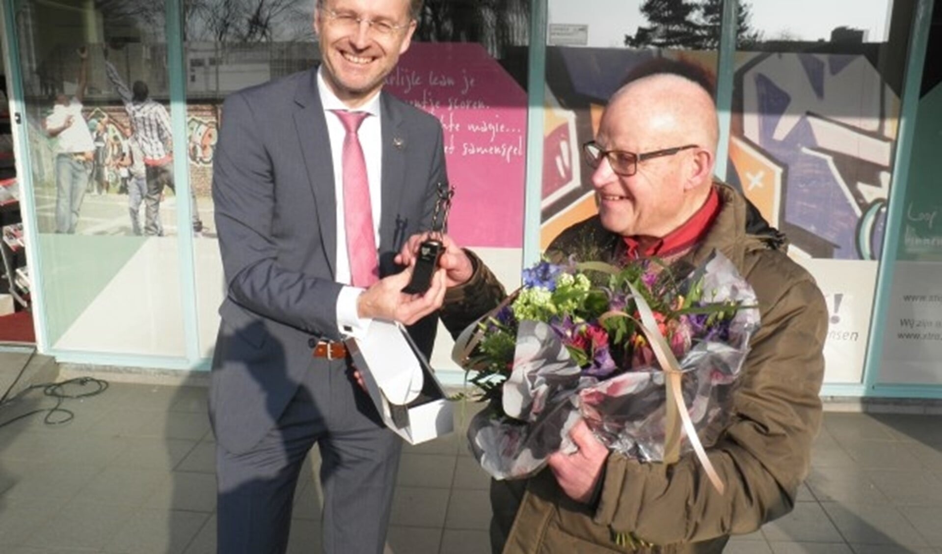 Wethouder Robin Paalvast overhandigt Theo Hulsker het beeldje en bloemen voor zijn jarenlange inzet. Foto Kees van Rongen