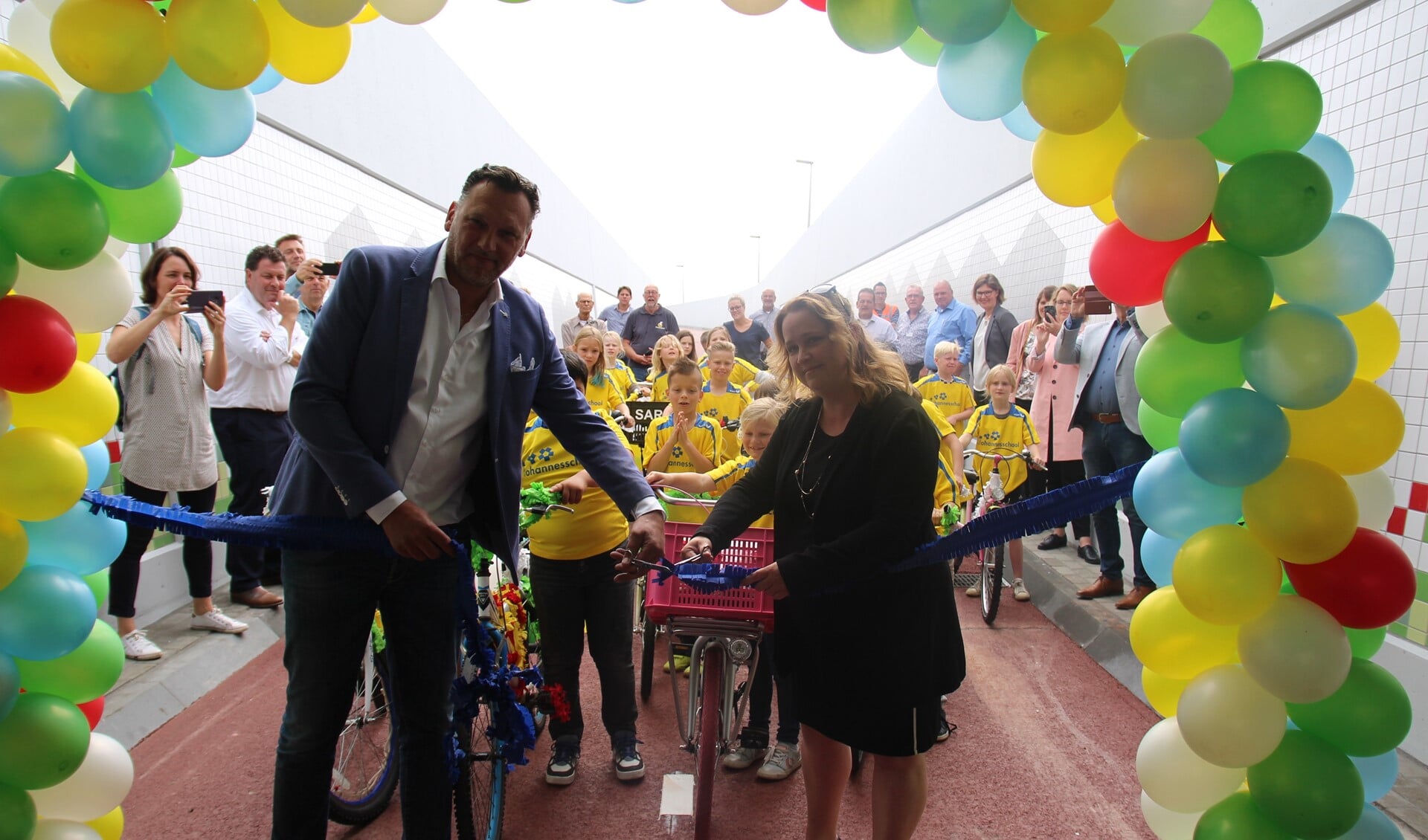 Wethouder Ilona Jense en Huib van der Ven van het gelijknamige aannemersbedrijf knippen een lint door en daarna kunnen de leerlingen van de Johannesschool de tunnel fietsend openen. 