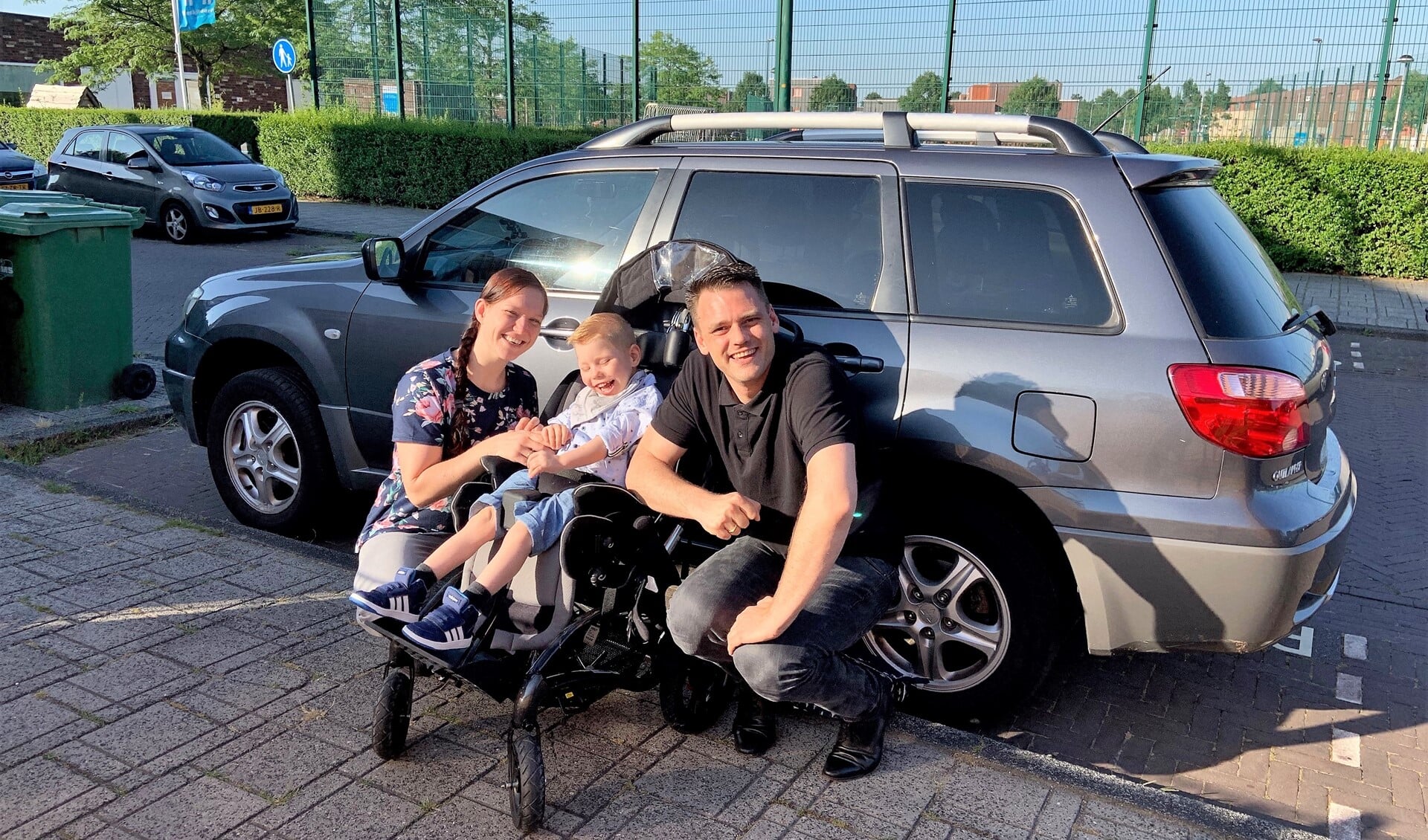 Sjors met papa en mama bij de auto die eigenlijk te klein is om zijn elektrische rolstoel in te kunnen vervoeren (familiefoto).