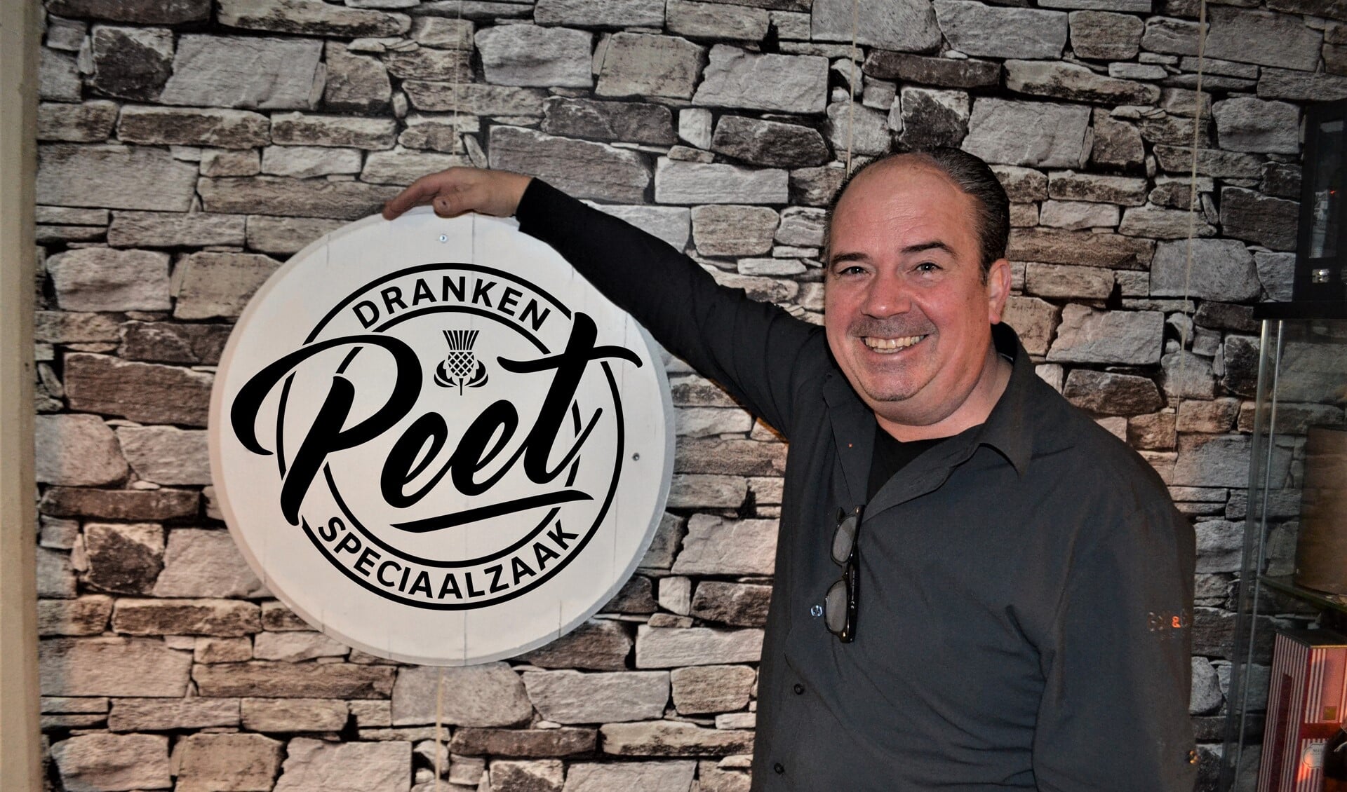 Peter Verbeek naast het nieuwe logo van zijn zaak  Drankenspeciaalzaak Peet.