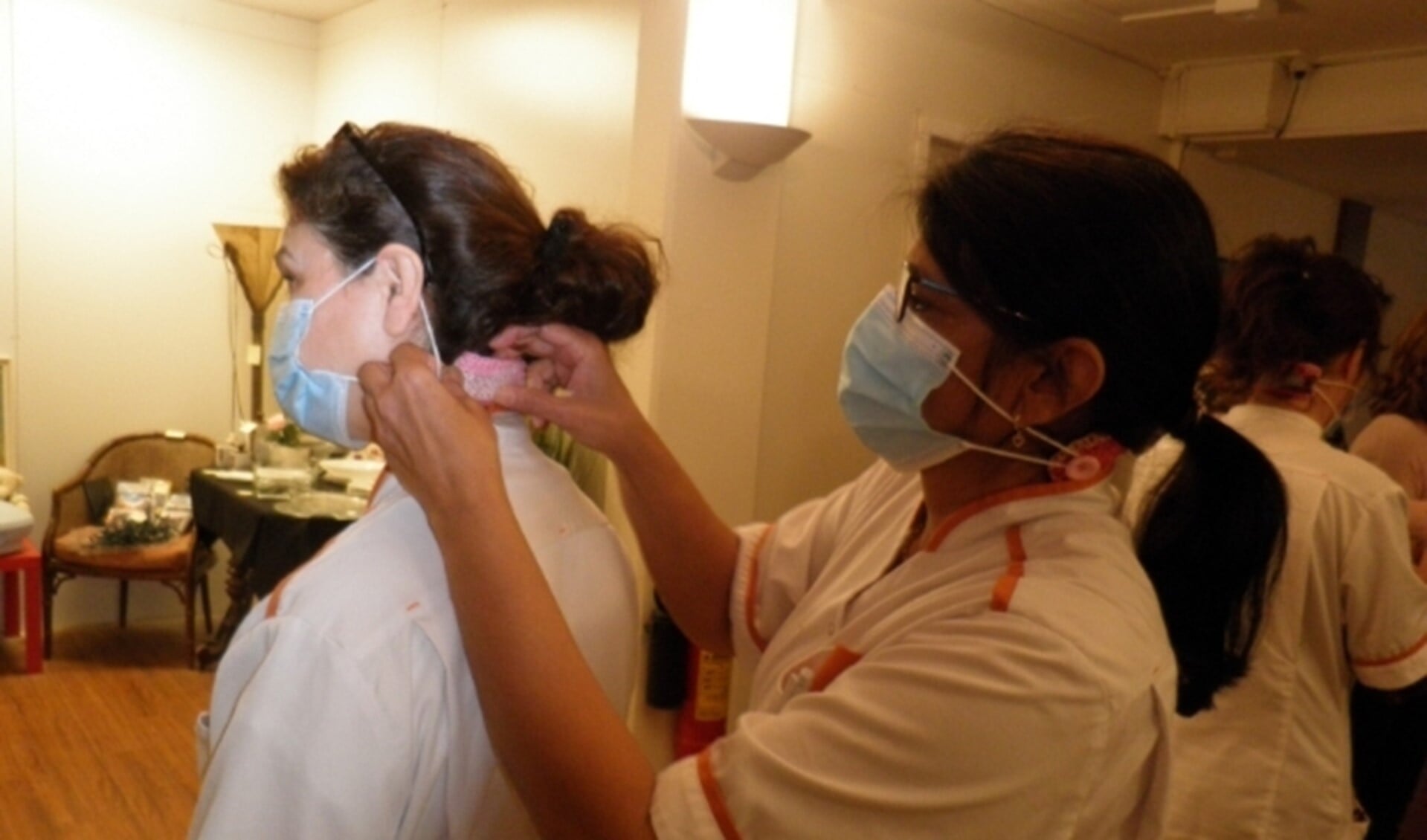 Zorgmedewerkers van WelThuis Buytenhaghe helpen elkaar met het vastmaken van de oorbuddy aan het mondkapje. Foto Kees van Rongen