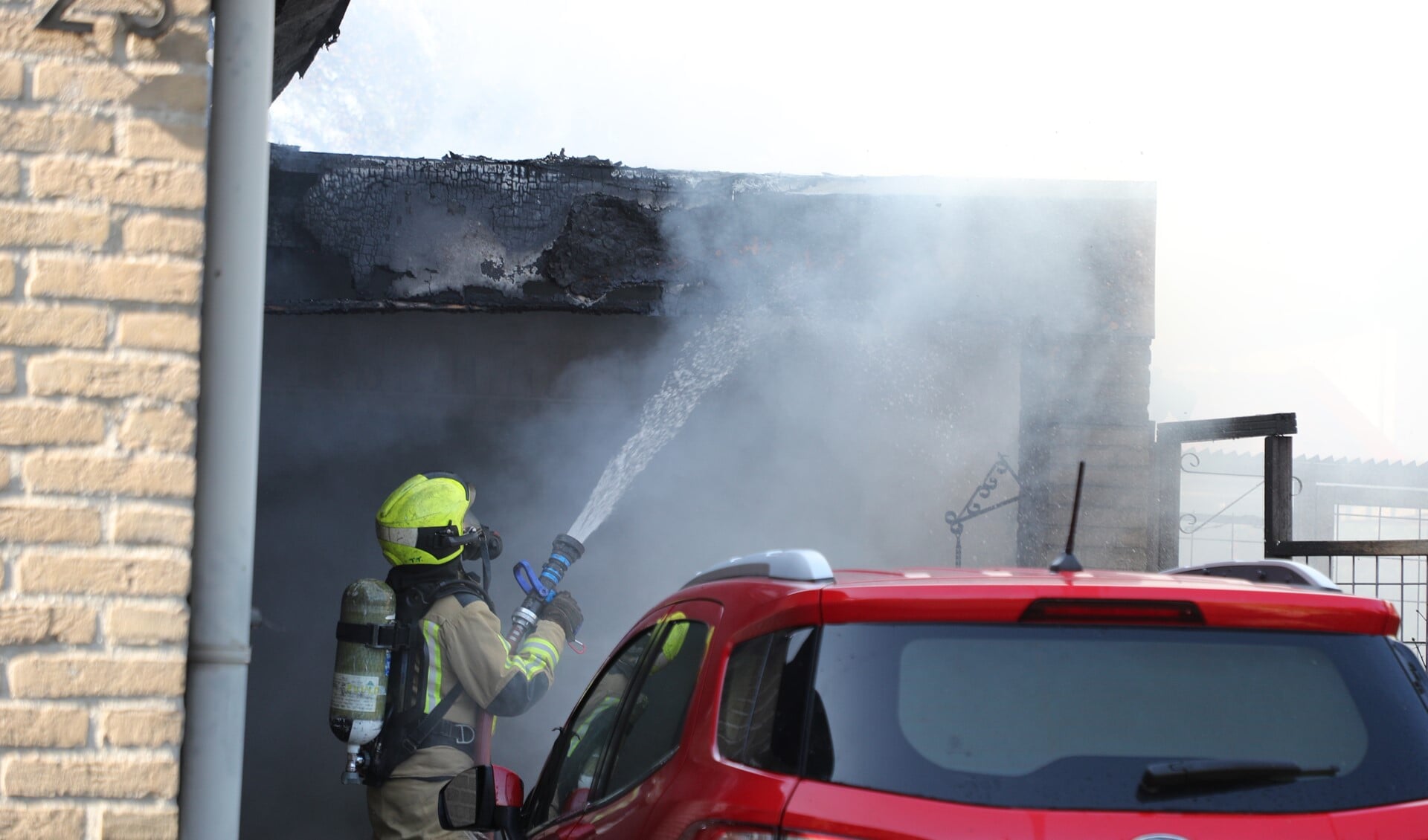 De brandweer blust na bij de brand in een garage naast een woning aan de Wickelaan (foto:Rene Hendriks).