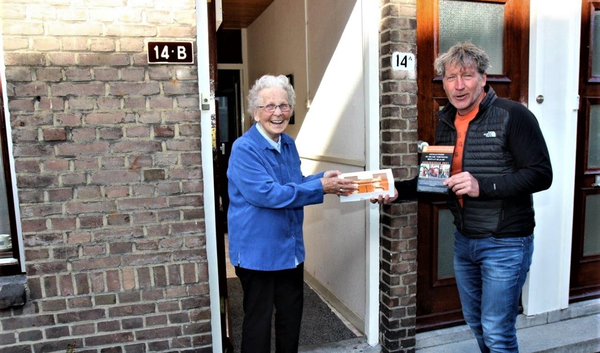 Voorzitter Erik van der Linden overhandigt aan mevr. Zaat, één van de oudste leden van de vereniging, een doos met oranjetompoezen (foto Ap de Heus)