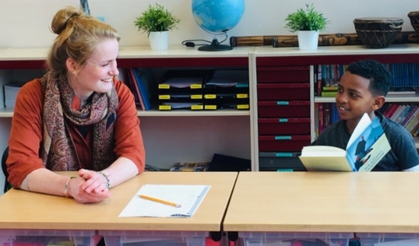 Een begeleider en leerling lezen samen een boek