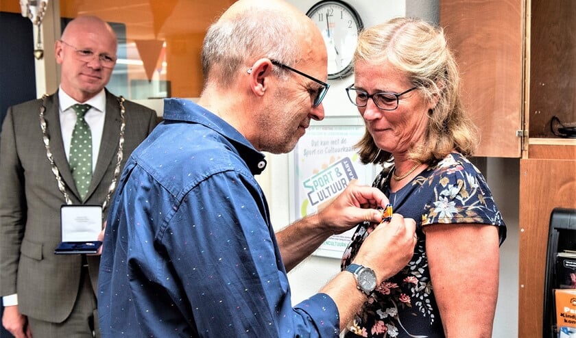 <p>De onderscheiding wordt Renie Luteijn opgespeld door haar echtgenoot terwijl de burgemeester toekijkt (foto: Michel Groen).</p>