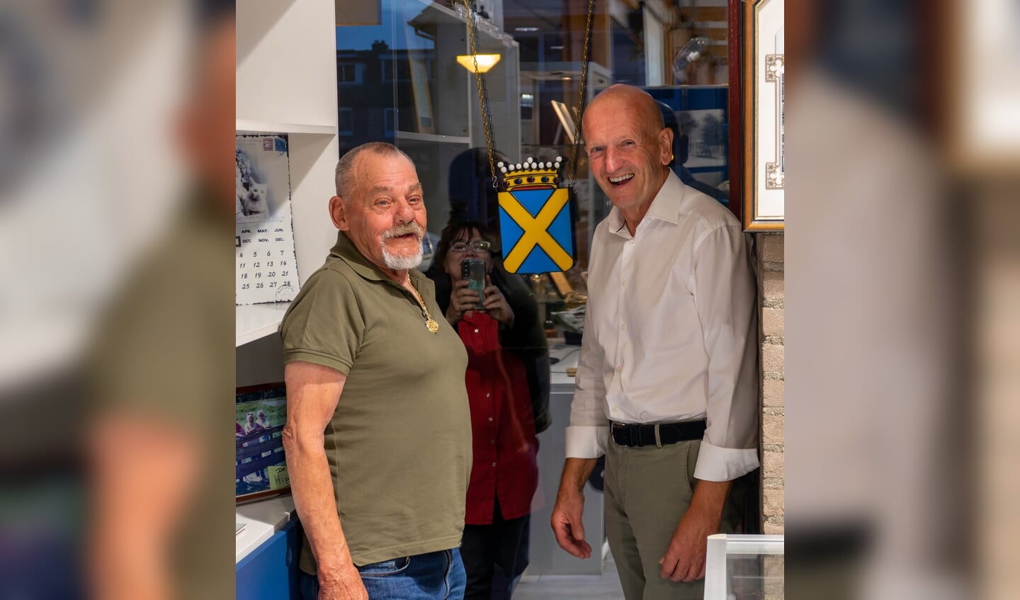 Het vroegere gemeentewapen van Pijnacker in Tiffany wordt door de maker, de bekende Bert van Tilburg, opgehangen samen met voorzitter Paul van Winden.