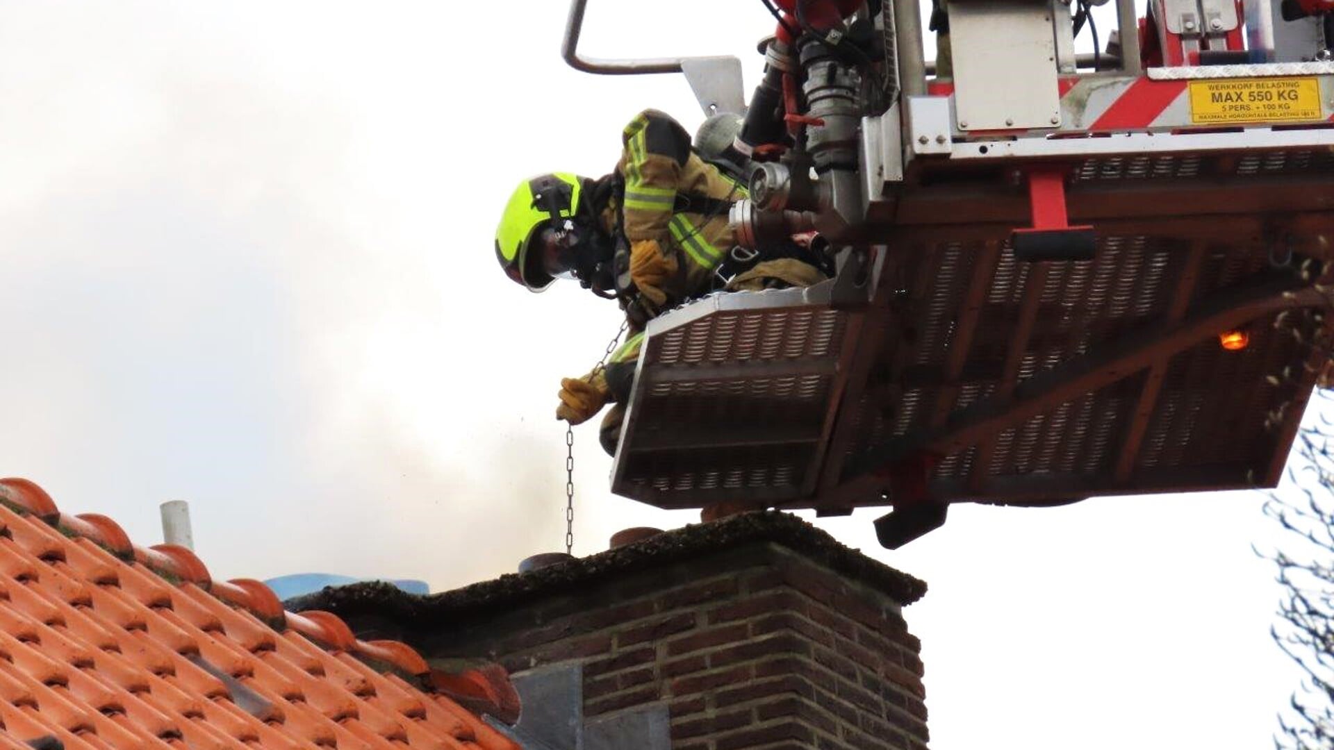 Een brandweerman is bezig de schoorsteen te ramoneuren  om het lastige brandje te kunnen blussen (foto: Ap de Heus).