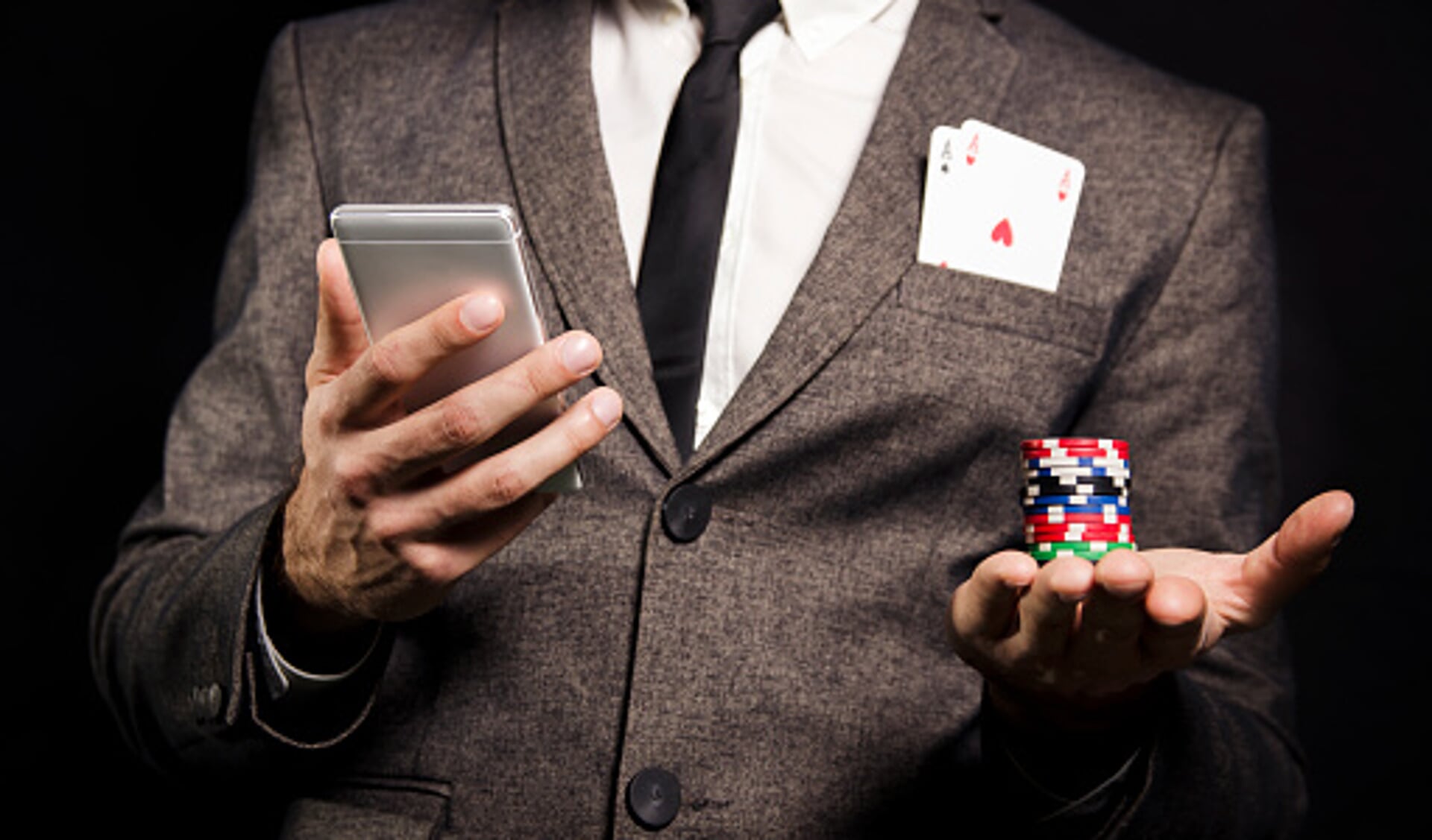 Man in suit with to aces in pocket holding poker chips and smartphone/ online poker