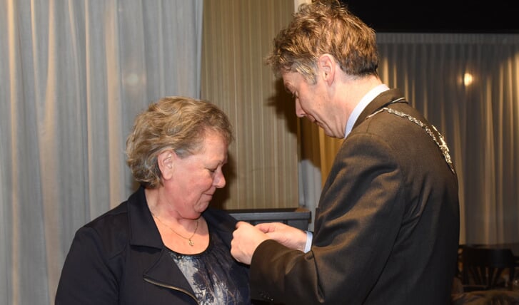 Burgemeester Hans Gilissen spelt de onderscheiding op bij Ria Flinsenberg-Steeghs. Foto: Hoedemaekers.