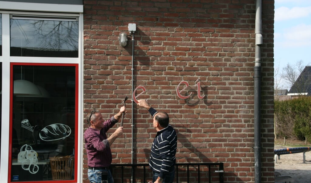 Toon van Osch en Wil Cornelissen verwijderen de oude letters 'De Hei' van de voormalige basisschool.