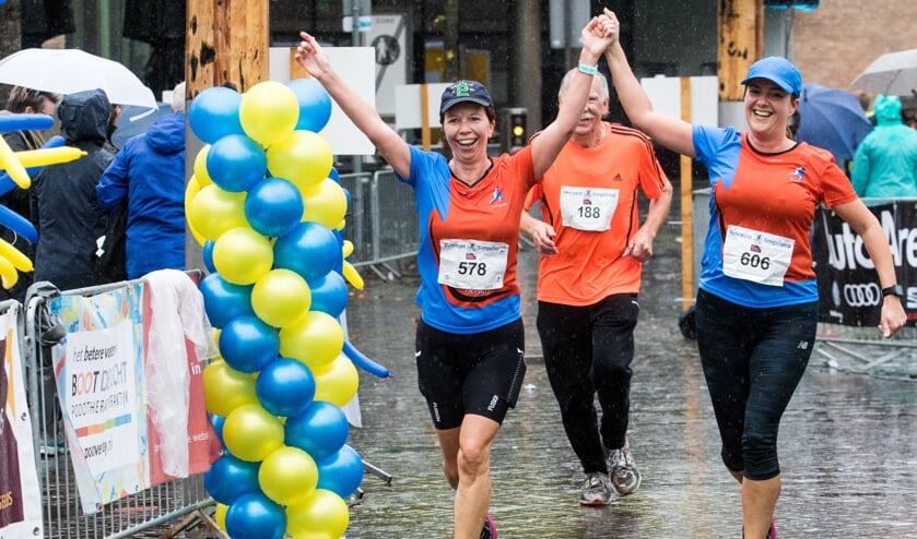 Charlotte (links) en Yvon komen samen juichend na tien zware kilometers door de regen over de finish.