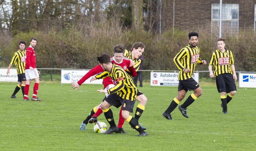 SV Oostrum-aanvaller Chris Wilschut (rood shirt) probeert twee spelers van BVV'27 af te schudden.