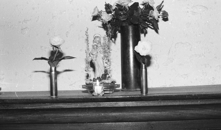 Een foto van een beeldje omringd door kogelhulzen gevuld met bloemen.